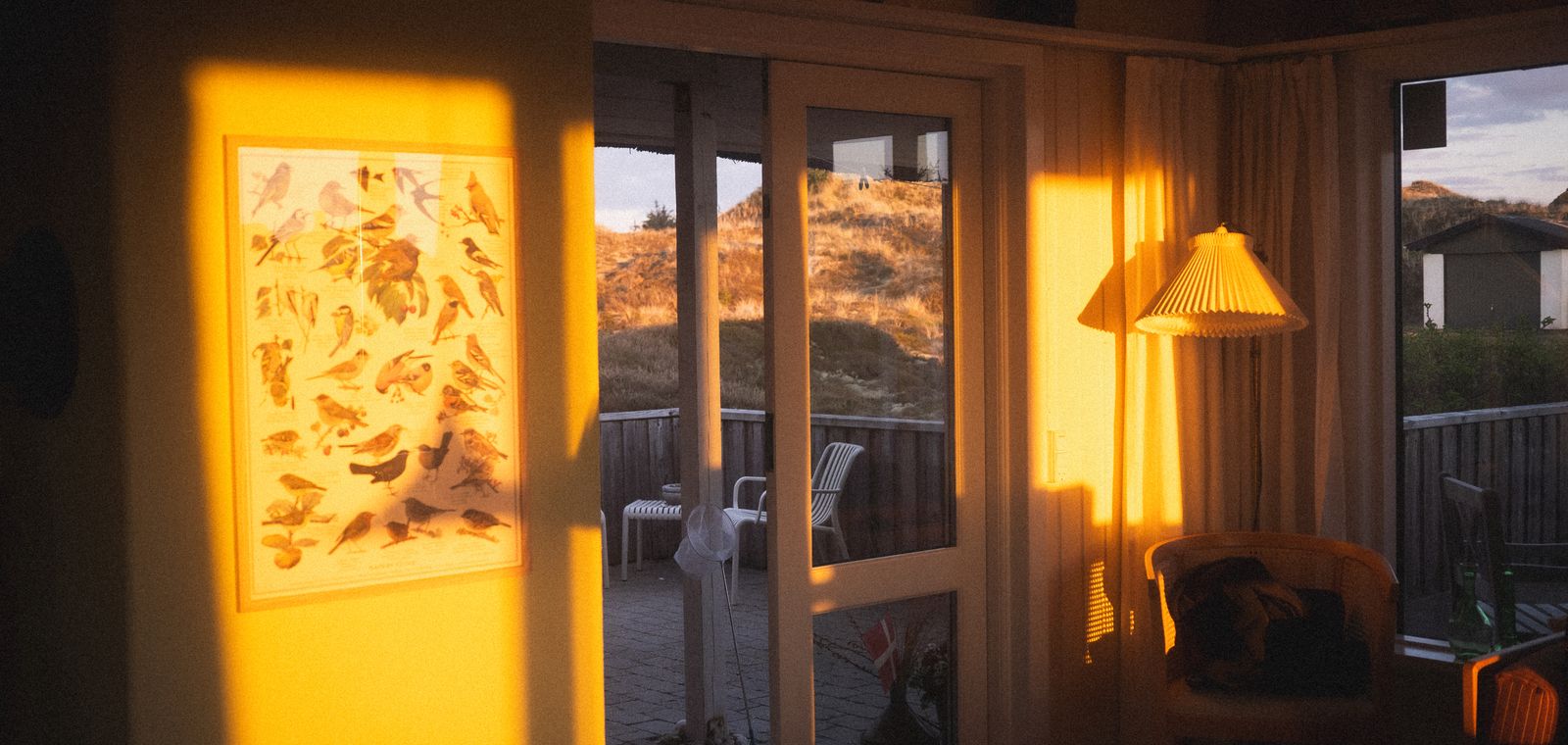A living room at golden hour, warm light spilling across the walls and a lamp glowing in the corner